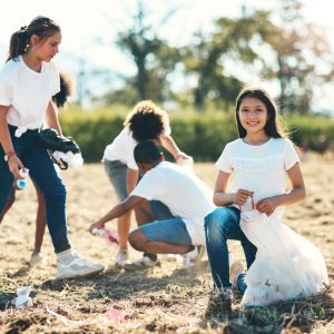 Shot of a group of teenagers picking up litter off a field at summer camp.